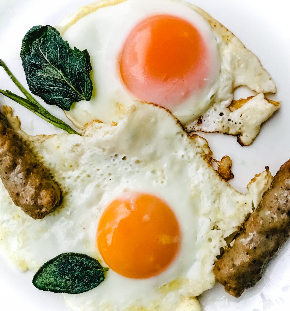 A plate of sunny side up eggs with crispy whole sage leaves and breakfast sausage links