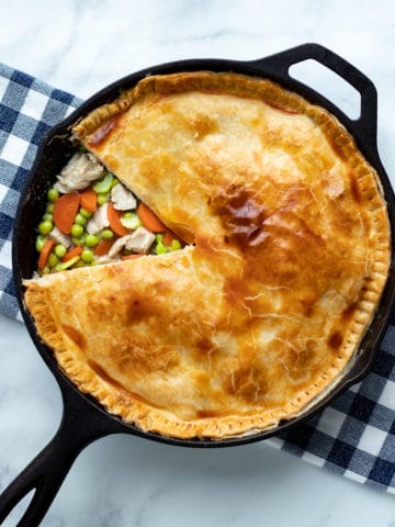 Easy low carb chicken pot pie baked in a cast iron skillet with a wedge cut from the top crust so you can see the filling of chicken peas and carrots and gravy