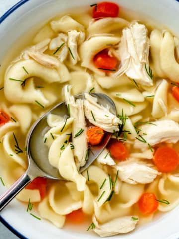 A closeup look into a nice bowl of homemade chicken noodle soup with carrots and a few snips of fresh dill.