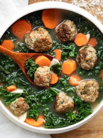 A bowl of Italian wedding soup is a pairing of bite-sized garlicky meatballs in a light broth with green kale and carrots.