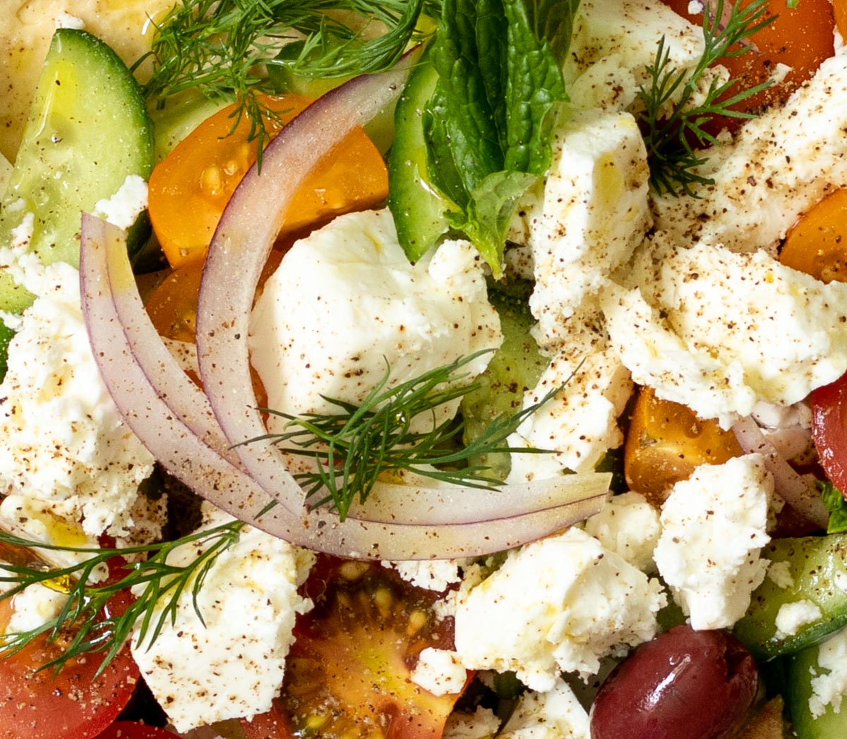 close up of Cucumbers, tomatoes, onion, feta cheese, olives, mint, dill, olive oil and lemon juice