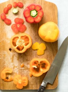 Red and orange bell peppers on a cutting board with tops and bottoms removed next to a knife.