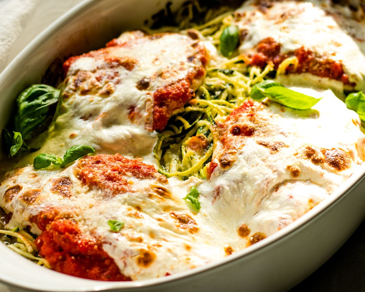 4 pieces of chicken parmesan baked in a casserole with spiralized zucchini