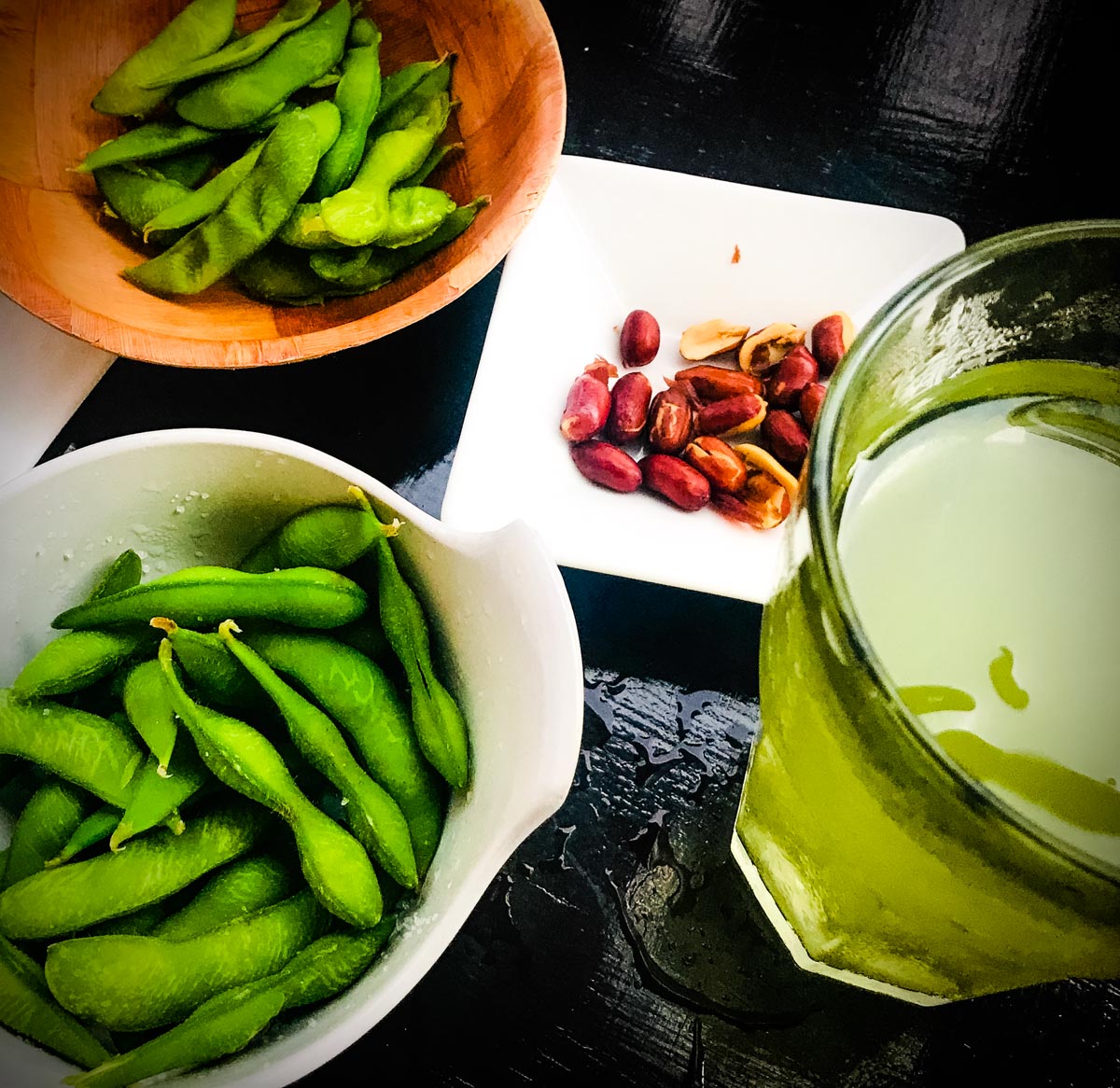 Bright green edamame soy beans in pod served with roasted peanuts and iced green tea
