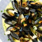 Mussels in creamy, buttery white wine sauce on a plate with sliced garlic and chives