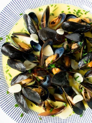 Mussels in creamy, buttery white wine sauce on a plate with sliced garlic and chives