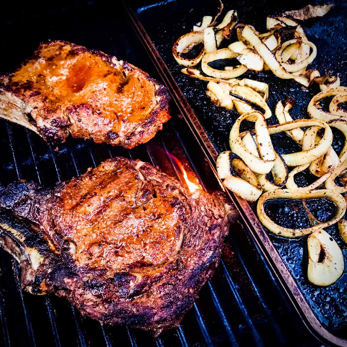Outback steakhouse style rib-eye steaks on a grill with a griddle of onion rings