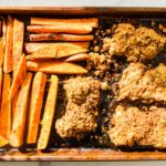 Peanut crusted oven fried chicken thighs on a baking sheet with cajun sweet potato fries