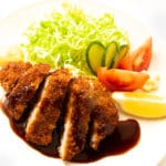 Japanese-style pork cutlet (tonkatsu) on a plate with sauce lemon wedge and vegetables