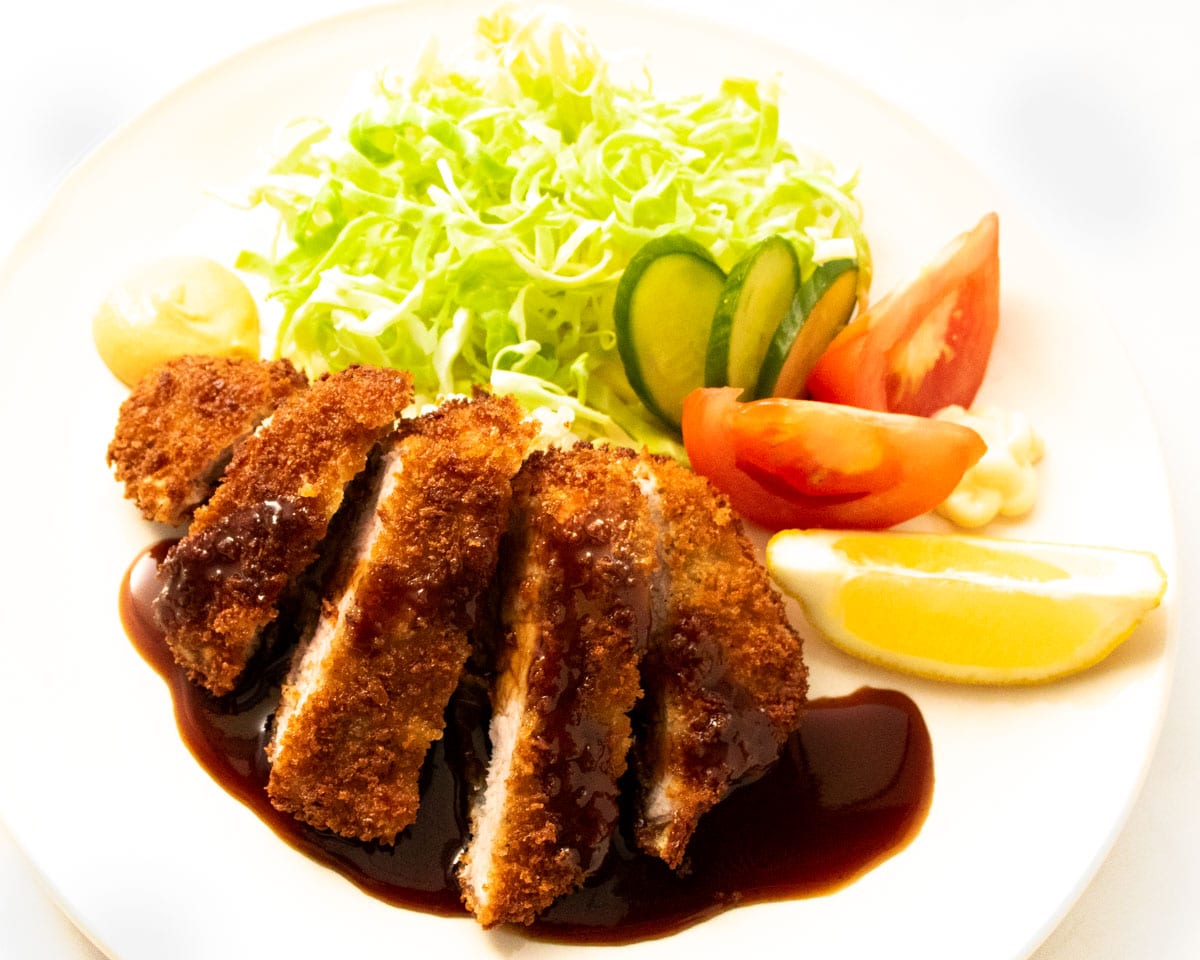 Plate of tonkatsu or Japanese fried pork cutlet served with brown sauce and a side of fresh cabbage and a lemon wedge