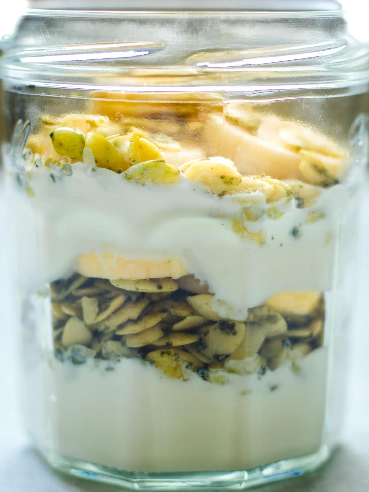Side view of yogurt parfait layered with banana and salted pumpkin seeds in a mason jar