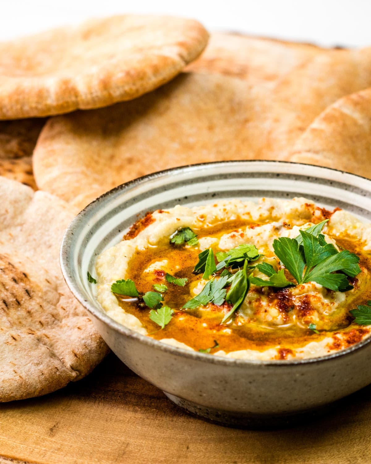 portrait view of a bowl of baba ghanoush surrounded with mini pita bread rounds 