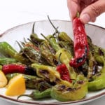 Pan roasted shishito pepper being lifted from a plate of peppers