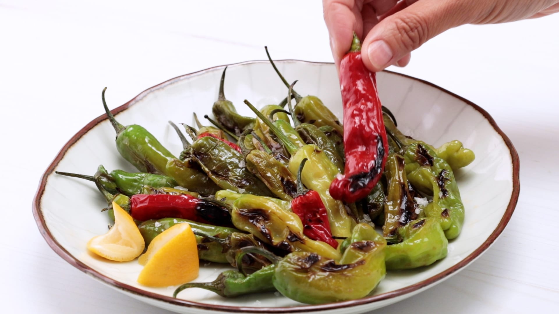 hand picking up a flash-fried blistered shishito pepper from a serving plate