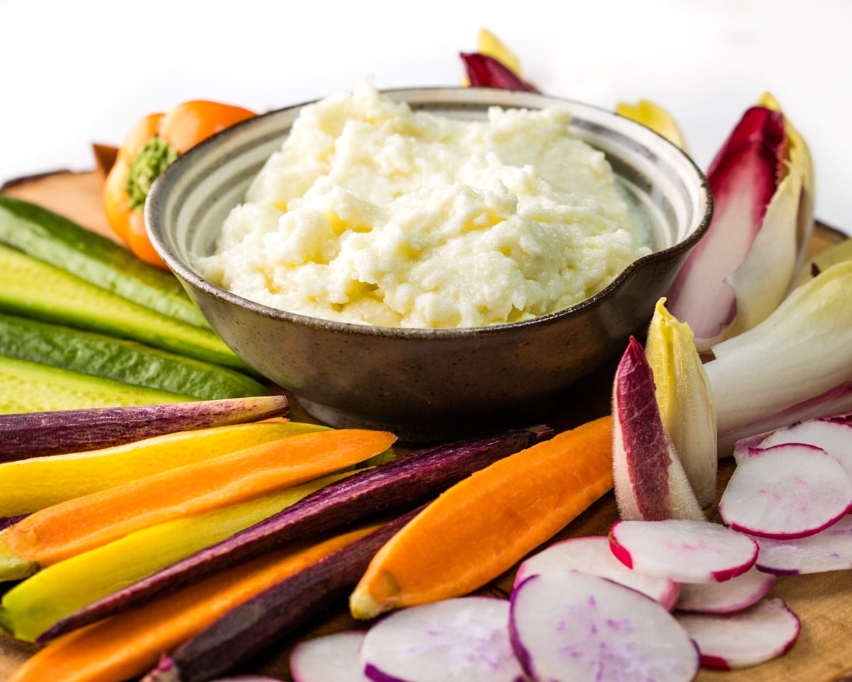 Toum is a Lebanese Garlic Sauce in a bowl and surrounded by carrots cucumbers endives and peppers for dipping