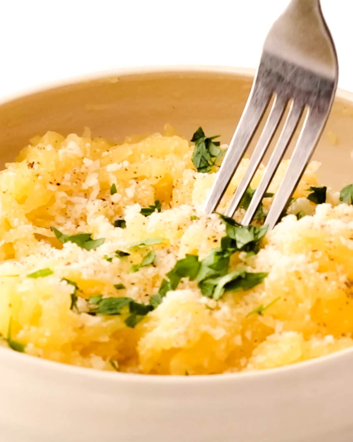Spaghetti squash with butter, Parmesan cheese, parsley and black pepper in a ceramic bowl with a fork dipping in for a bite