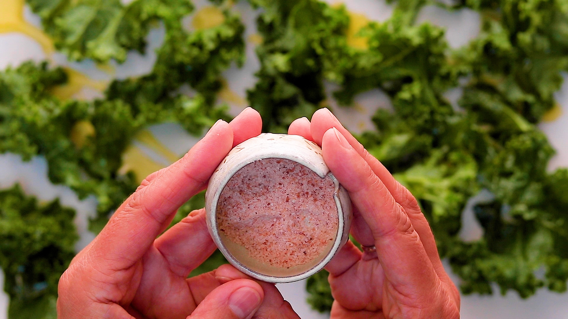 Pink Himalayan sea salt in a small ceramic container about to be spread over the kale. 