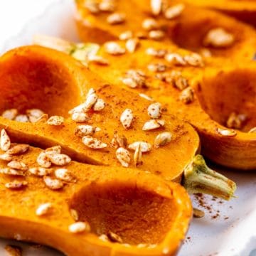 Four Roasted honeynut squash halves cut side up on a platter sprinkled with cinnamon and roasted honeynut squash seeds