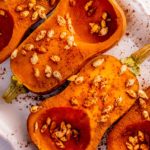 An overhead view of roasted honeynut squash halves garnished with toasted seeds