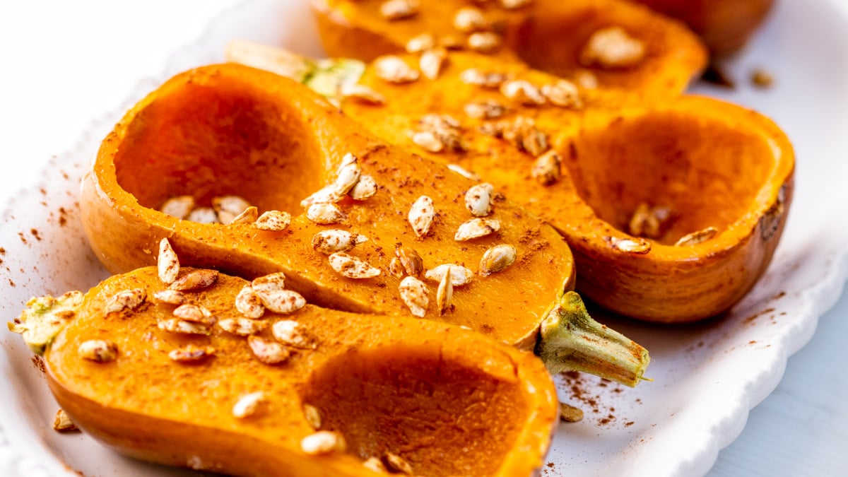 Four roasted honeynut squash halves cut side up on a platter garnished with powdered cinnamon and toasted honeynut squash seeds