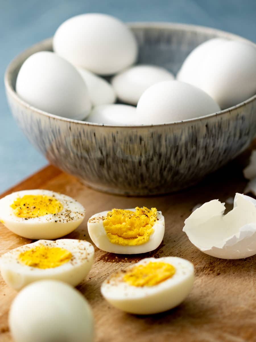 Bowl of hard boiled eggs with one peeled perfectly and halves showing yolks