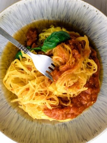 Air fryer spaghetti squash noodles plated with pasta sauce and garnished with basil with noodles twirled around a fork