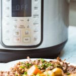 A tall platter of Instant pot pot roast in the foreground with an Instant pot in the background