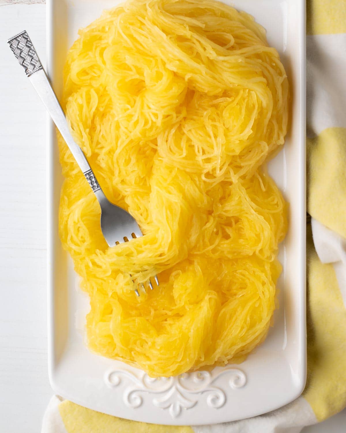 Spaghetti squash noodles from a whole squash on a platter with pretty dish cloth