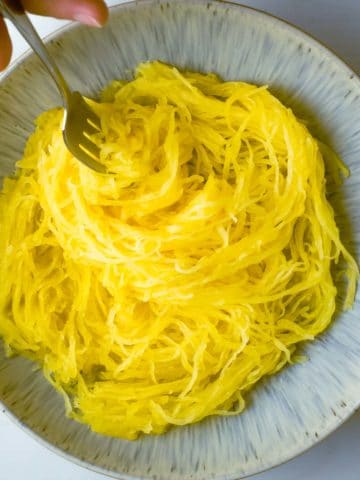 Instant pot spaghetti squash plated in a bowl with a fork twirling the squash "noodles"