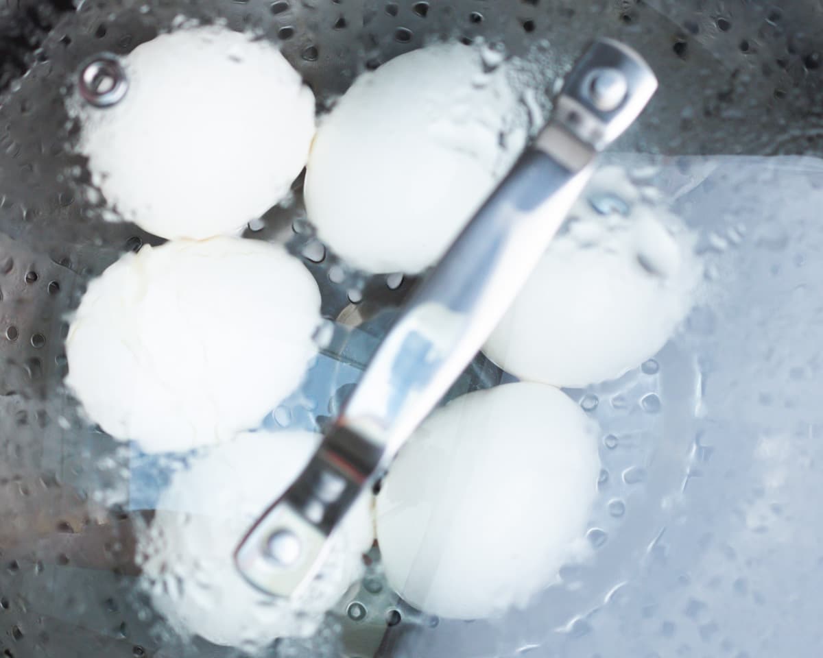 Raw white eggs steaming in a steamer basket on a cooktop