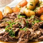 Instant pot pot roast with gravy featured image of shredded pot roast on a platter with carrots and potatoes garnished with chives