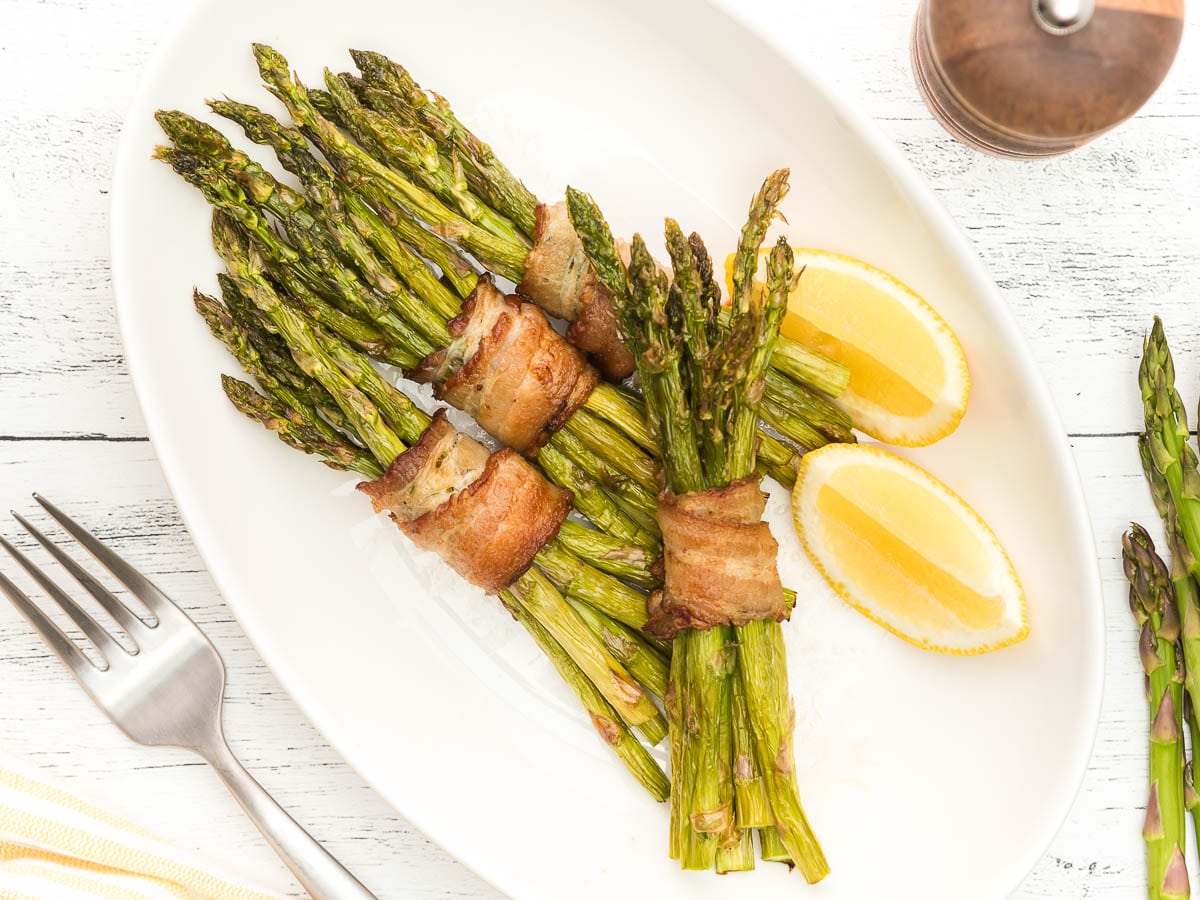 perfectly crispy air fryer bacon wrapped asparagus plated with lemon wedges