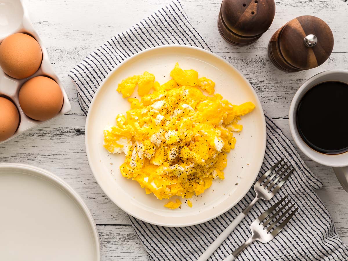 air fryer scrambled eggs on a plate wide view with eggs, salt and pepper shaker and cup of black coffee