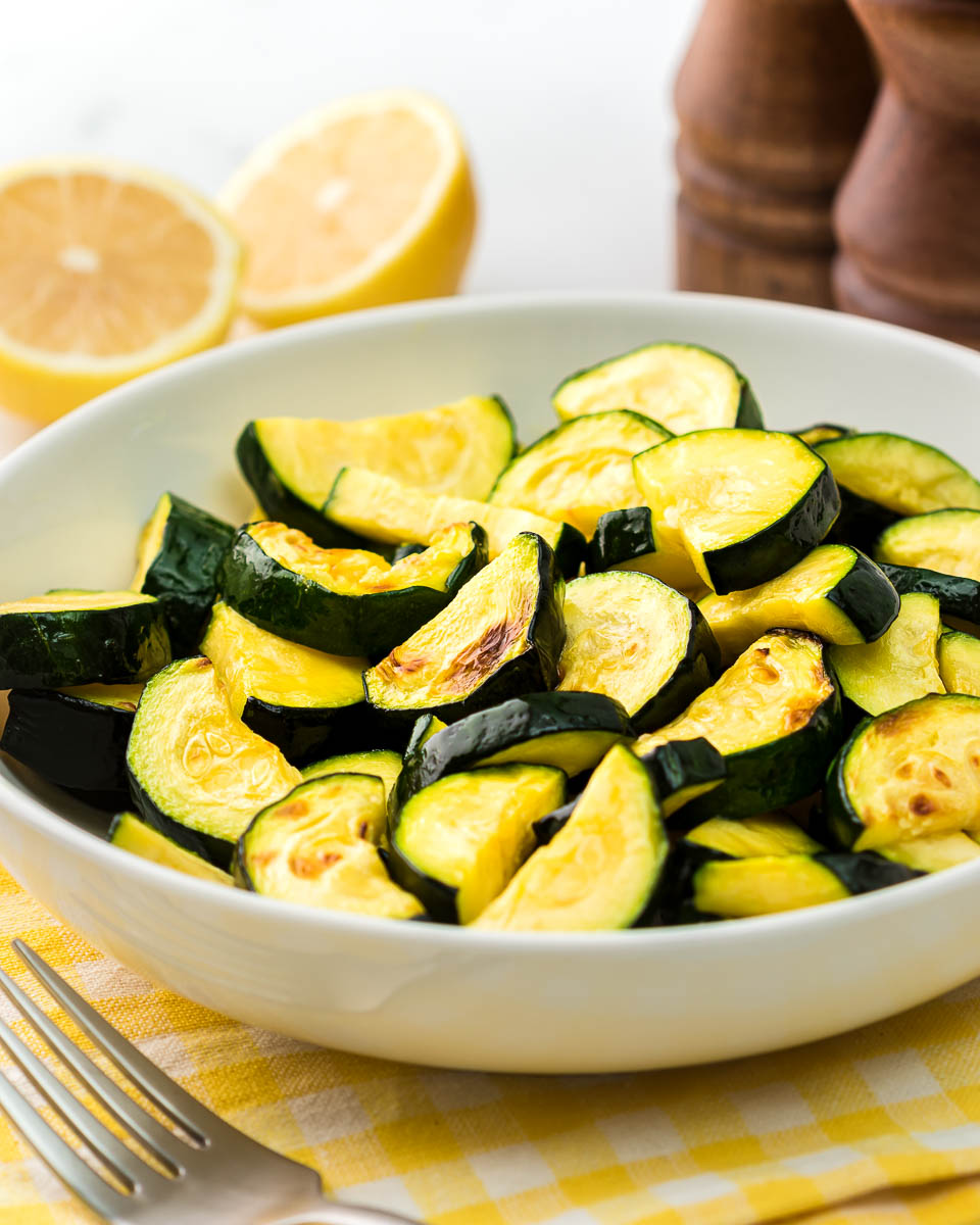 Air fryer zucchini in a bowl with fork and lemons