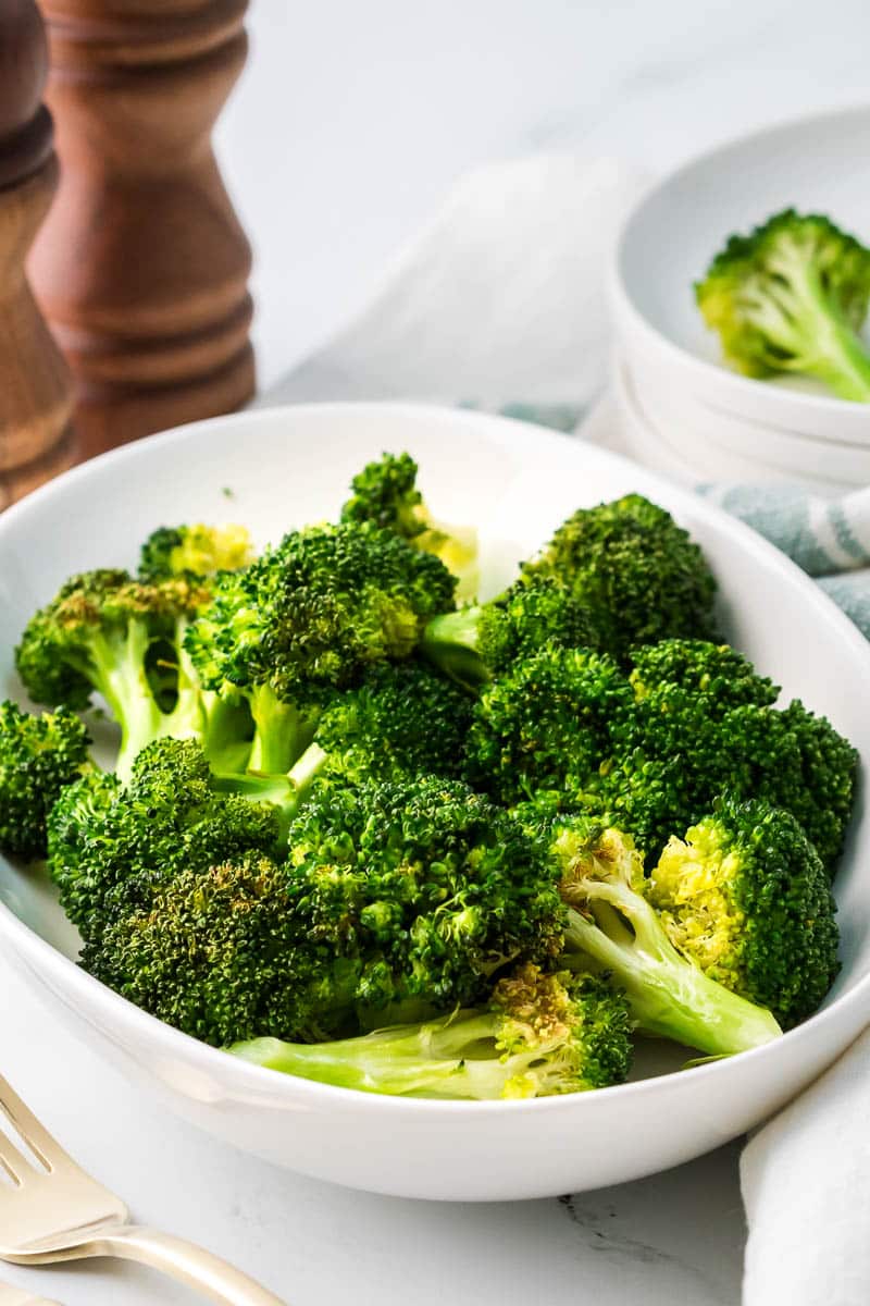 Air fryer broccoli served on a white platter with fork, napkin and salt and pepper shakers and plates