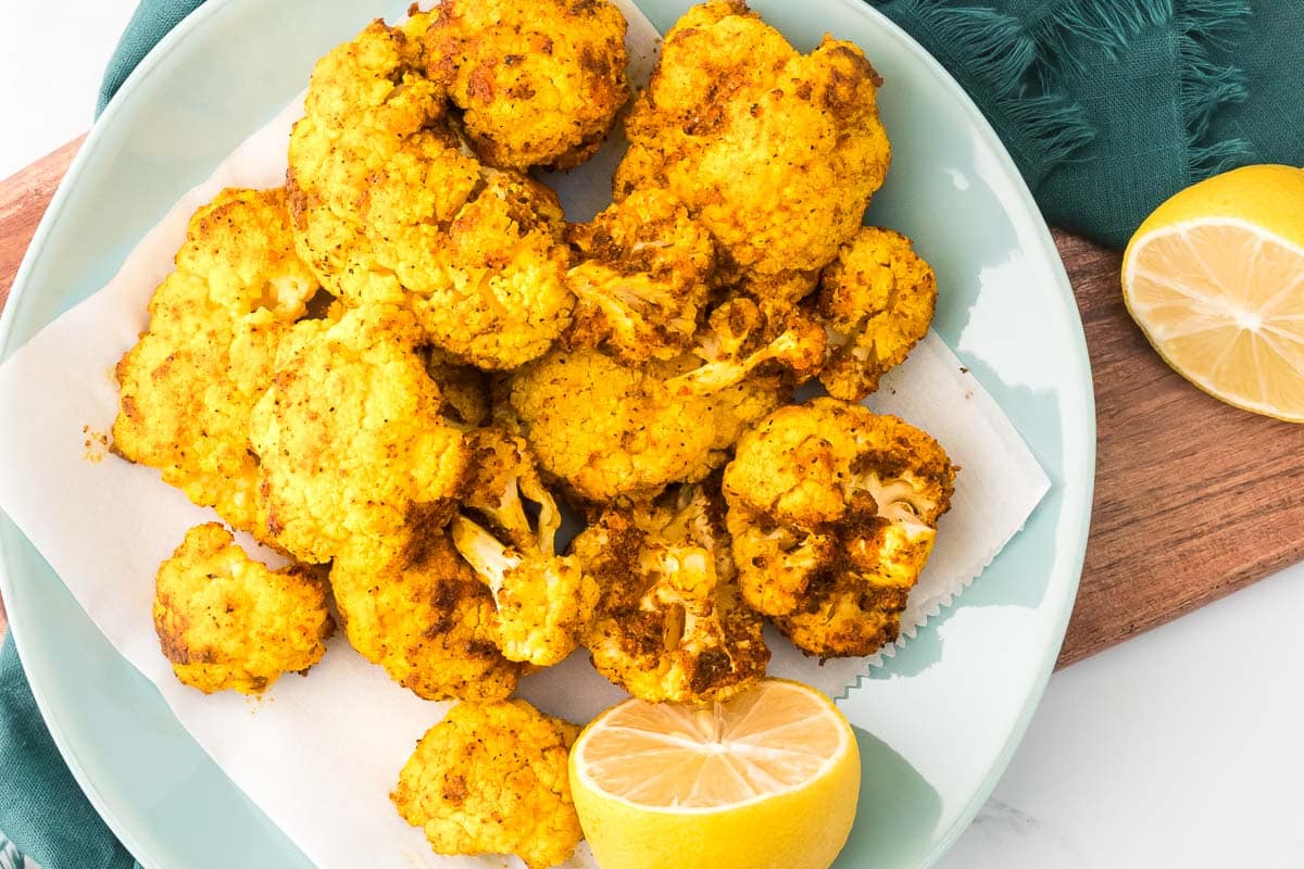 Air fryer cauliflower plated with lemons on a board with a napkin overhead view