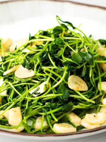 side shot of Pea shoots on a plate with sliced garlic