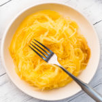 Baked spaghetti squash closeup on white plate with a fork in the center