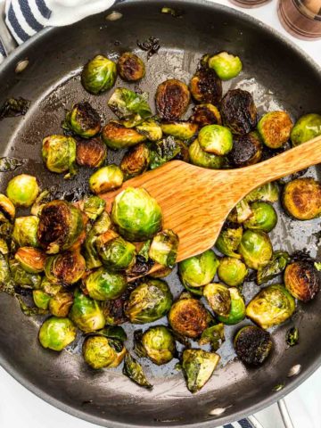 Balsamic glazed Brussels sprouts in a non stick skillet with wooden spatula