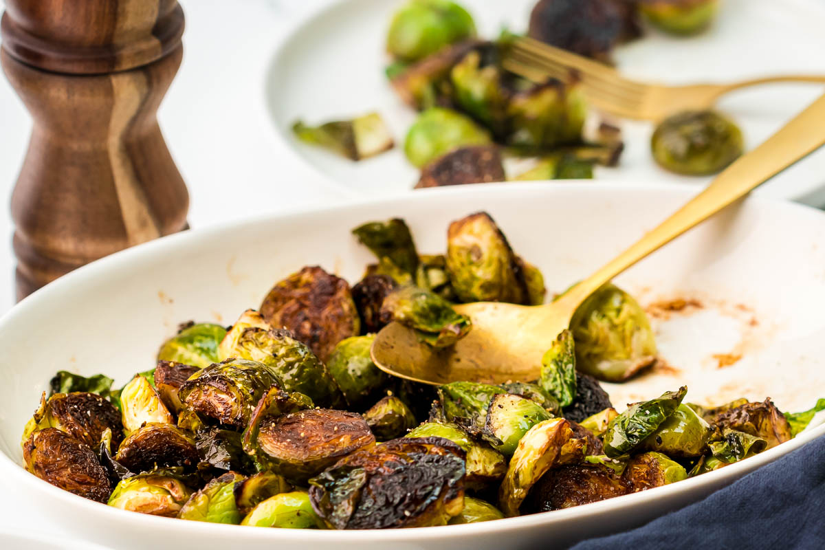 Balsamic glazed Brussels sprouts served on a platter and plated with fork in background